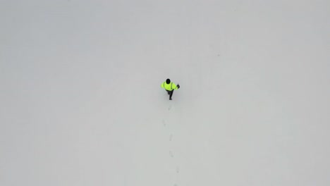 Aerial-top-down-view-of-person-wear-green-safety-jacket-and-walk-on-frozen-field