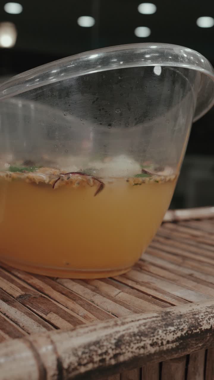 Plastic pitcher containing orange beverage with ice on wooden table - vertical