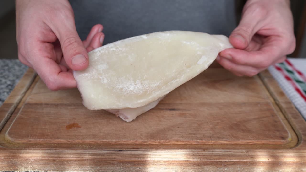 hombre sosteniendo calamar sin piel congelado en la tabla de corte