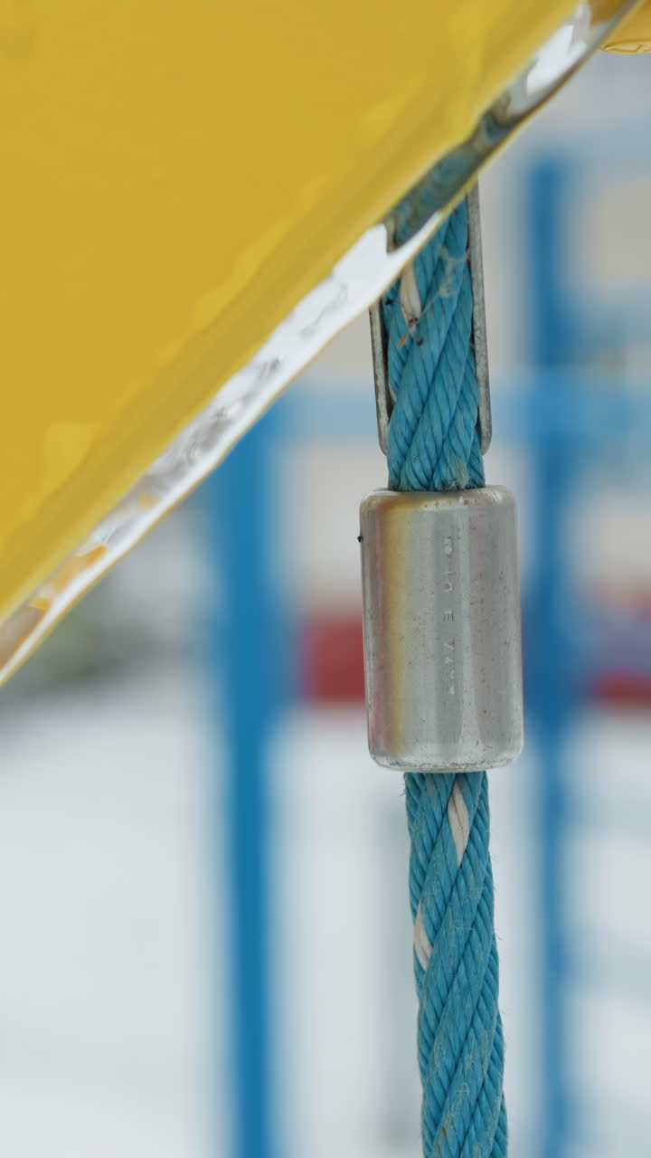 primer plano de un columpio amarillo y azul con detalles de helada en una cerradura de metal y una cuerda azul vibrante, el fondo sutilmente borroso con coloridos equipos de parque infantil