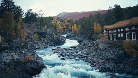 Water-Flowing-Through-Rocky-Stream-Passing-By-Cottage-During-Autumn-In-Dovrefjell,-Norway