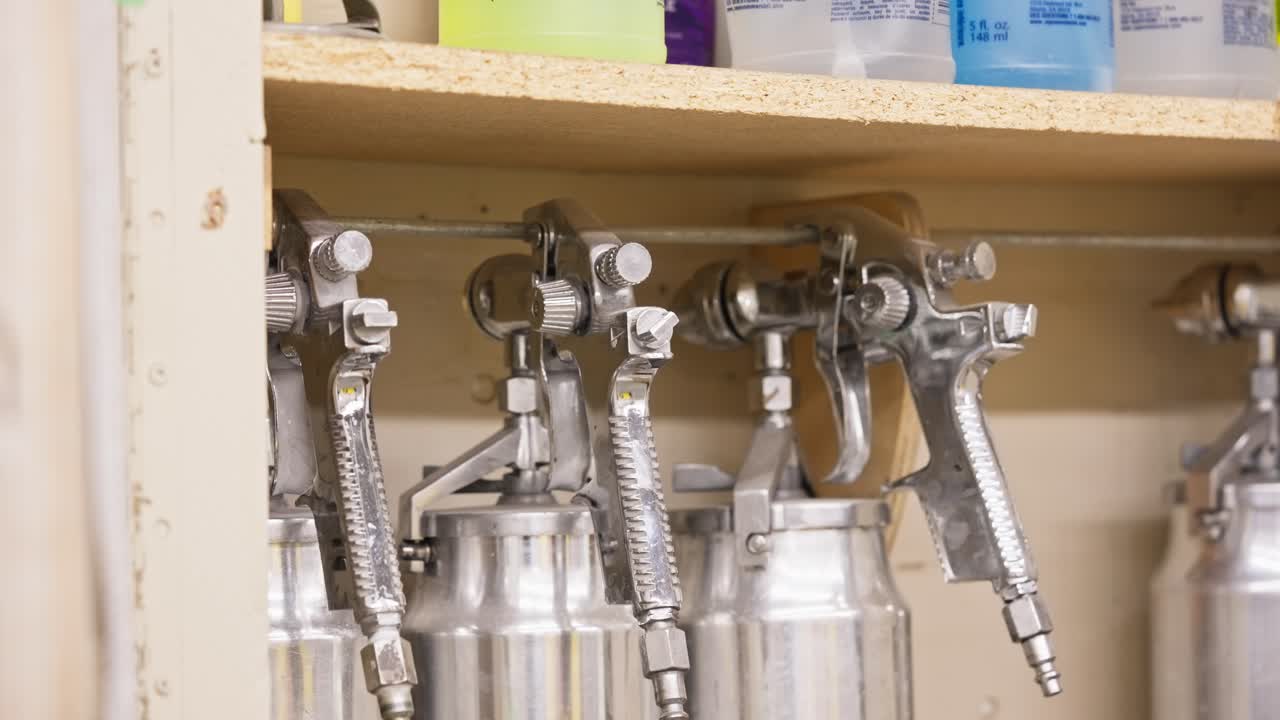 Zoom reveals row of chrome spray guns neatly arranged in an industrial shop