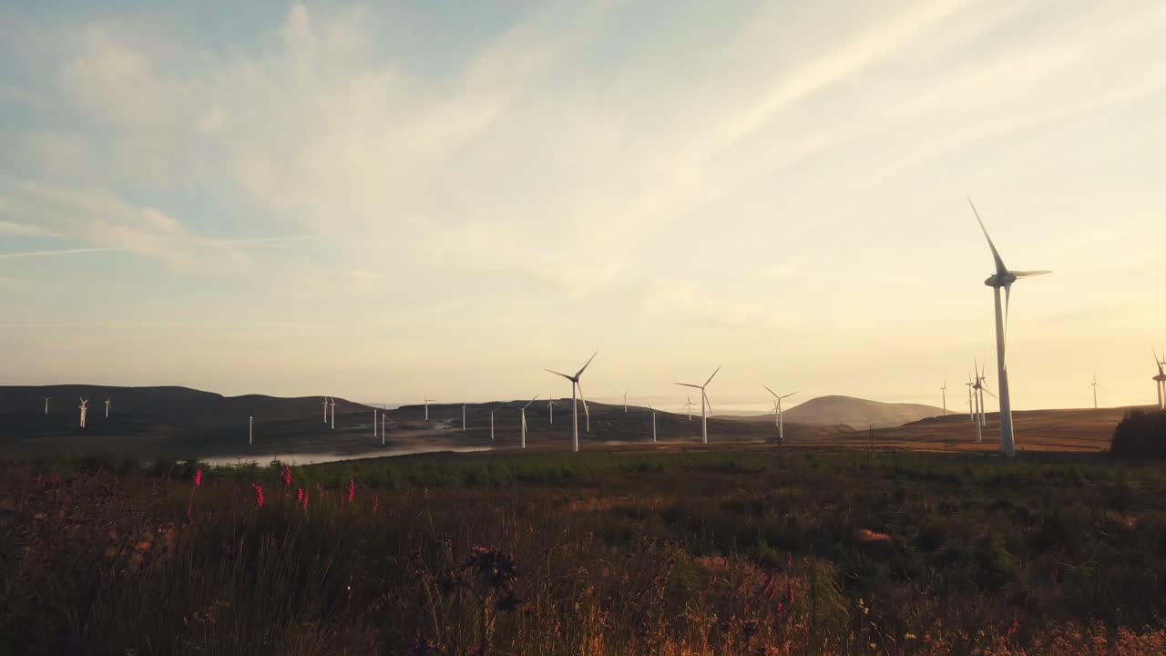 Landscape view of a windmill farm, producing green energy, cloudy and windy, at sunrise
