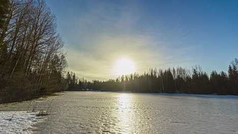 Static-shot-of-frozen-lake-surrounded-by-forest-on-a-cloudy-day-with-white-clouds-passing-by-in-timelapse