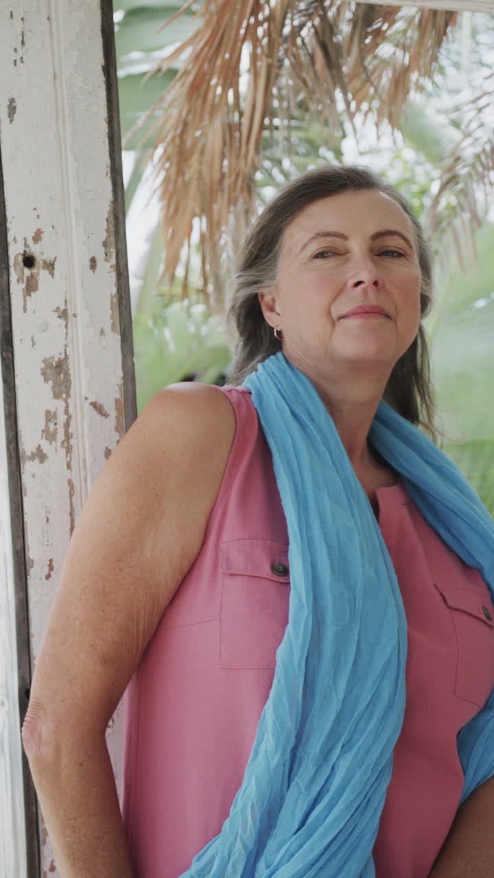 Vertical video portrait of happy senior caucasian woman relaxing on beach house porch, slow motion
