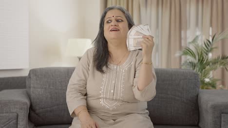 una anciana india feliz usando el dinero como ventilador.