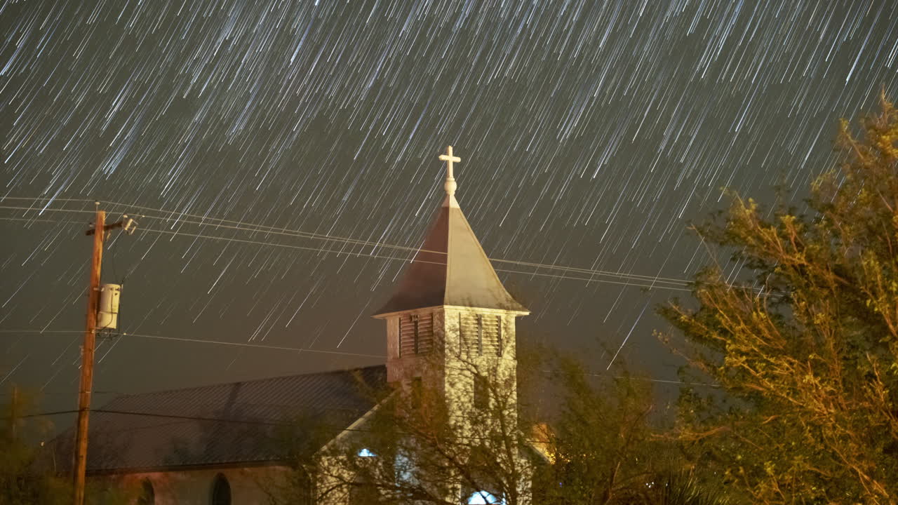 Stars trail in to comets drifting downwards over a small church steeple - Astro Time lapse