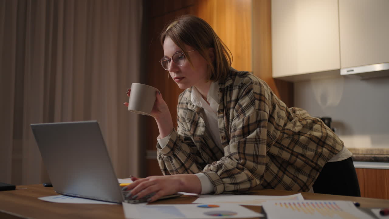 Beautiful young woman working on laptop computer while sitting at the living room drinking coffee. Happy casual beautiful woman working on a laptop. working at home with laptop and documents