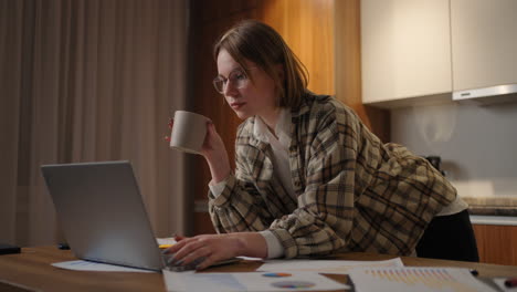 beautiful young woman working on laptop computer while sitting at the living room drinking coffee. happy casual beautiful woman working on a laptop. working at home with laptop and documents