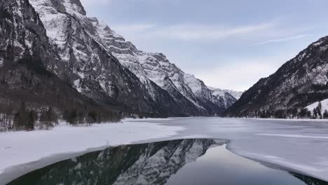 magnificent view of lake klöntalersee, half frozen and half reflecting the snow-covered mountains in its crystal-clear waters.