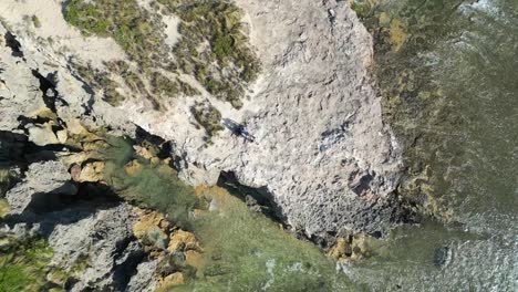 Sea-waves-splashing-on-the-rocky-coastline,-top-down-aerial-helix-shot