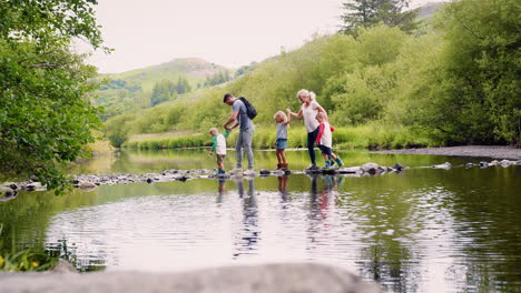 slow motion shot of parents helping children to cross river whilst hiking in uk lake district