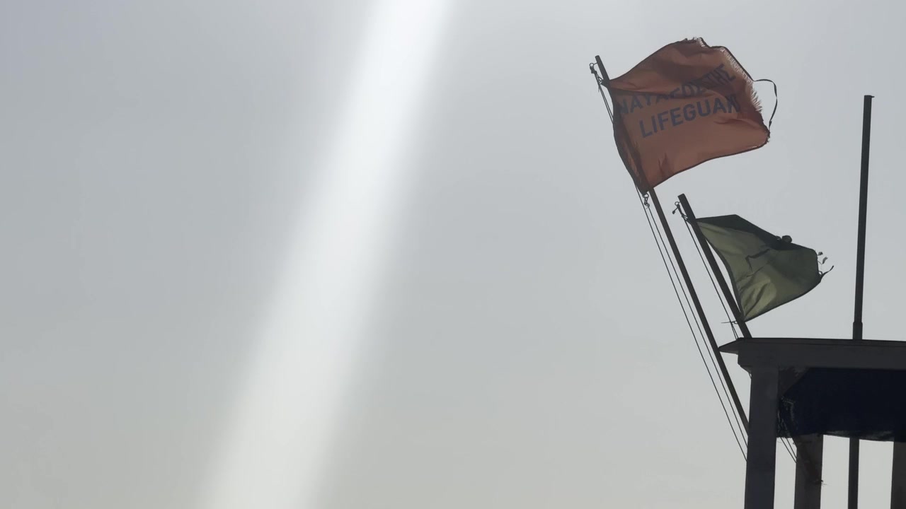 Close-up summer video of two lifeguard flags waving in the breeze against a bright blue sky in Greece.