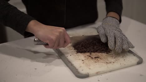 una joven coreana corta chocolate negro antes de derretirlo para hacer galletas de mantequilla millonarias mientras usa guantes de seguridad