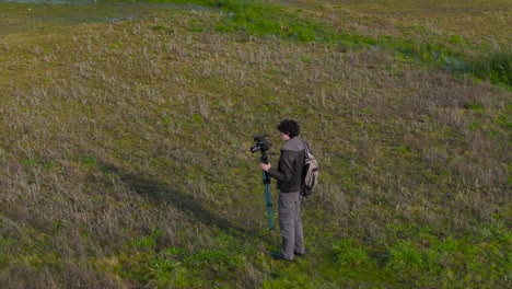 Männlicher-Fotograf-Mit-Kamera-Auf-Stativ-Auf-Dem-Feld-In-Der-Nähe-Des-Sees