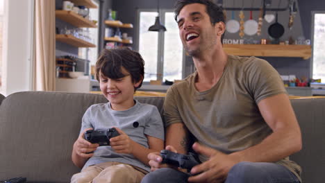 father and son sitting on sofa in lounge playing video game