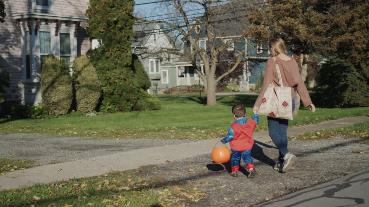 Parent leads by the hand a little boy in a costume, they go for candy on Halloween