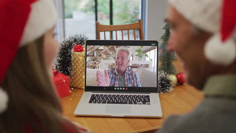 Rückansicht-Eines-Kaukasischen-Paares-Mit-Weihnachtsmützen,-Das-Während-Der-Weihnachtszeit-Einen-Videoanruf-Auf-Dem-Laptop-Führt