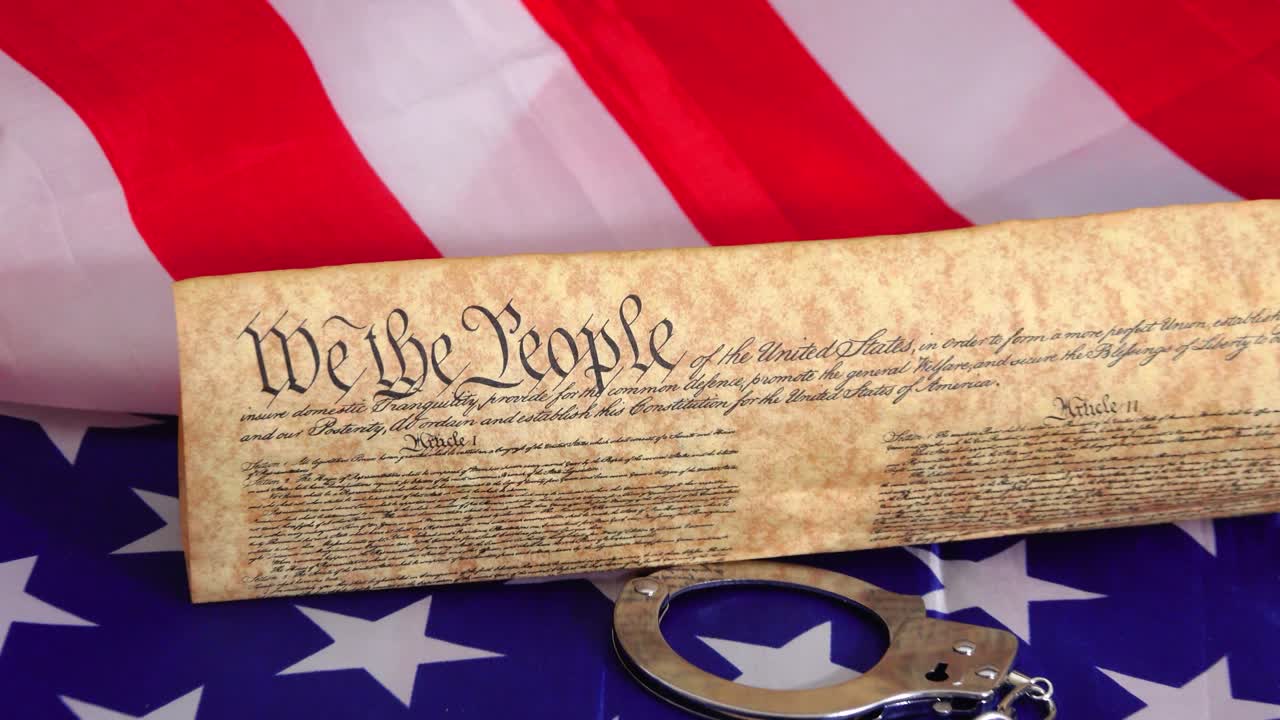 Symbolic image of handcuffs restraining the US Constitution against the backdrop of the USA flag representing the tension between freedom rights justice and the rule of American law