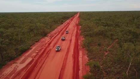antena: tiro de drones rastreando tres vehículos 4x4 conduciendo en convoy en la carretera de nivel de capa de tierra roja cerca de broome, australia occidental