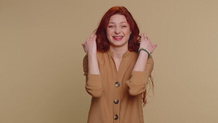 Donna dai capelli rossi, divertita e sorridente, che punta il dito verso la fotocamera, ridendo a crepapelle per una barzelletta o un aneddoto divertente.