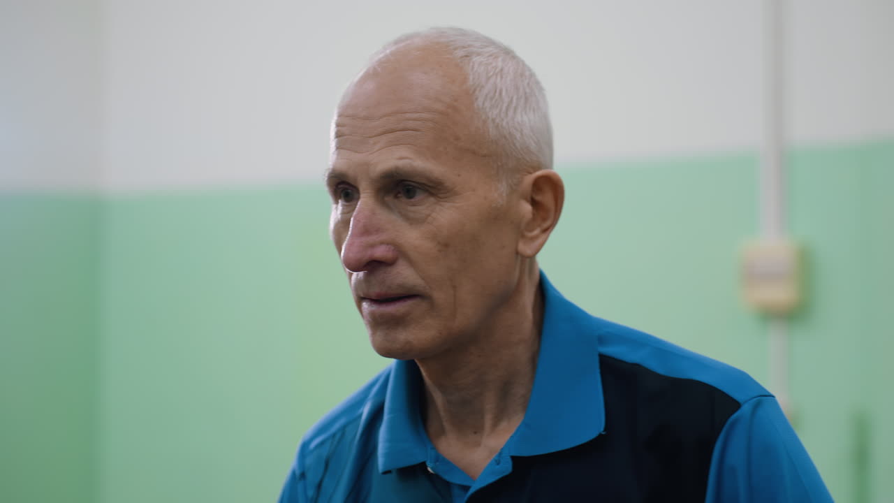 Close up of man in blue shirt engaged in table tennis match while interacting, with blurred indoor background showing light box on wall