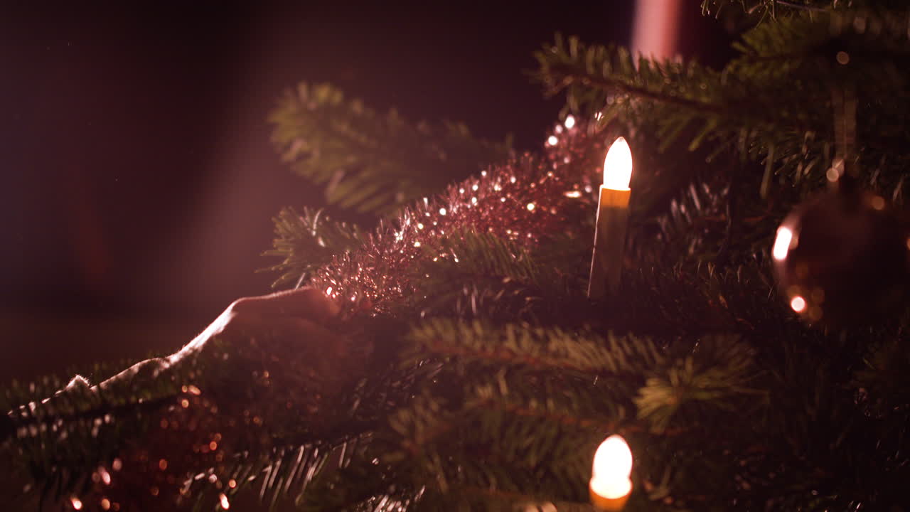 Nærbillede af kvindes hænder, der hænger glimmerpynt op på juletræet derhjemme