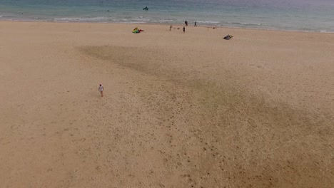 Vista-Aérea-De-Una-Playa-Con-Algunos-Kitesurfistas-Junto-Al-Agua-Jugando-Con-Las-Cometas