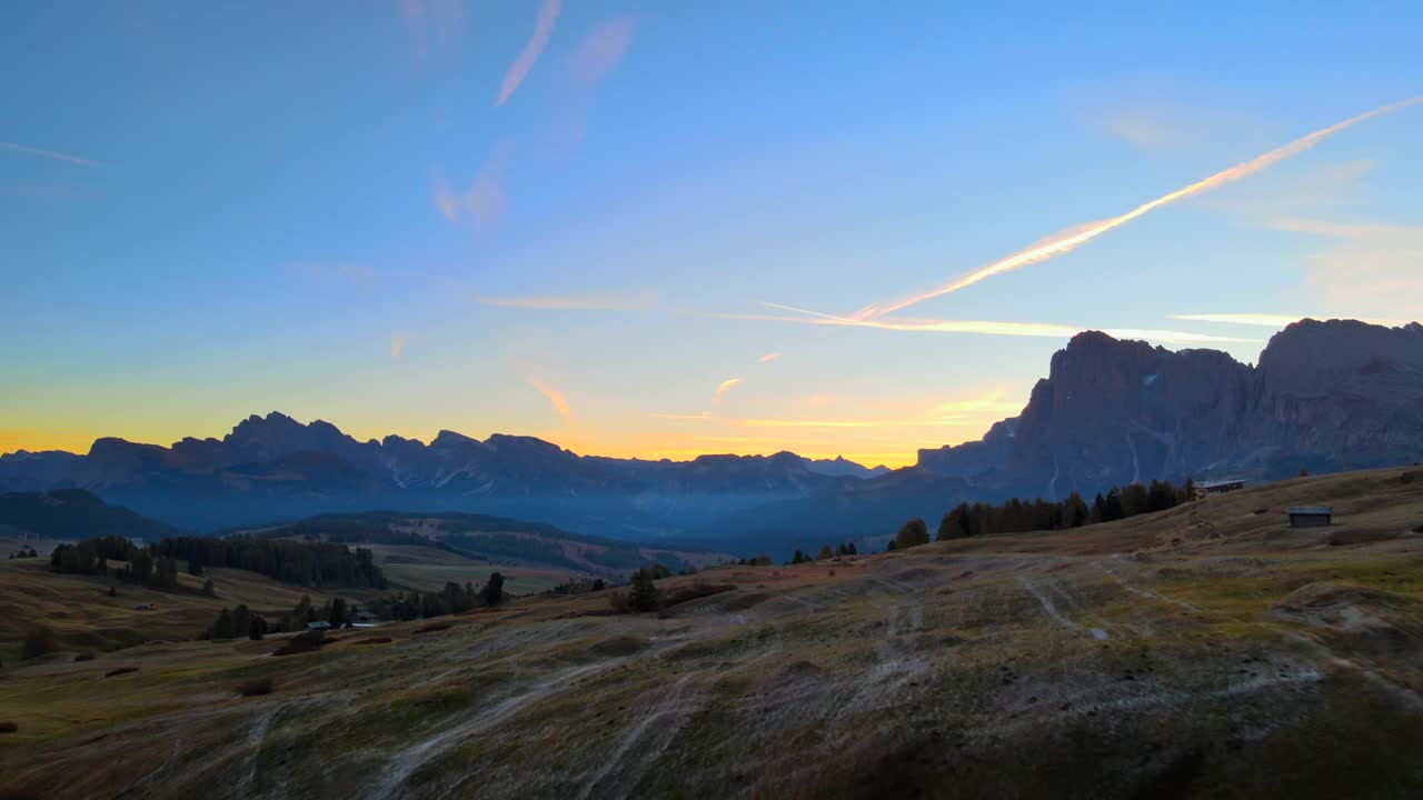 Mountains, forest and grass fields with wooden cabins filmed at Alpe di Siusi in Alps, Italian Dolomites filmed in vibrant colors at sunrise