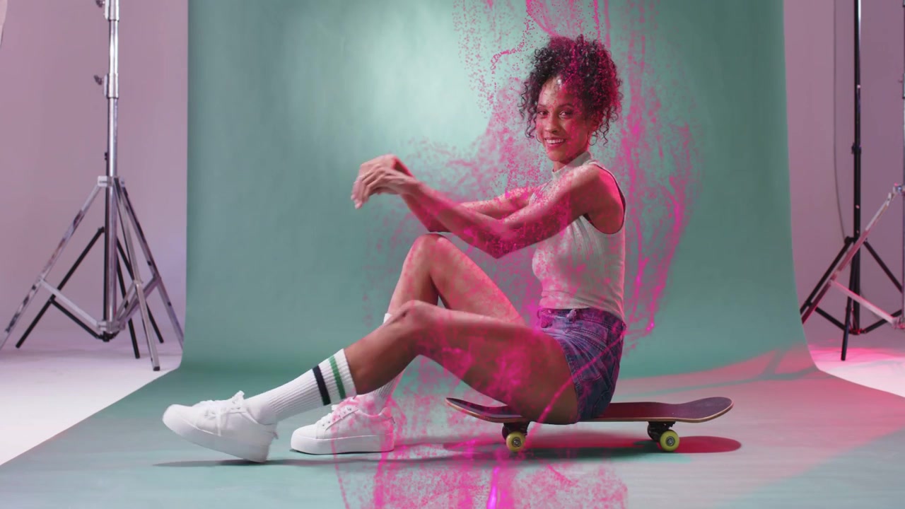 Photographer releasing pink powder, woman posing on skateboard for fashion shoot, brushing cloud
