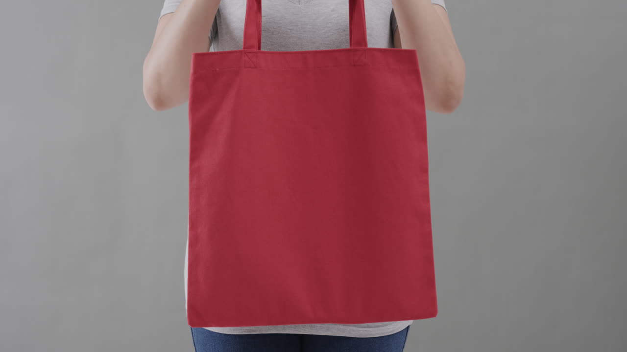 ⁇ 색 티셔츠를 입은 백인 여성이 회색 배경에 빨간 가방을 들고, 복사 공간, 슬로우 모션