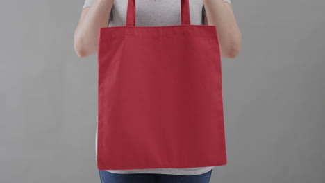 mujer caucásica con camiseta blanca sosteniendo una bolsa roja sobre un fondo gris, espacio de copia, cámara lenta