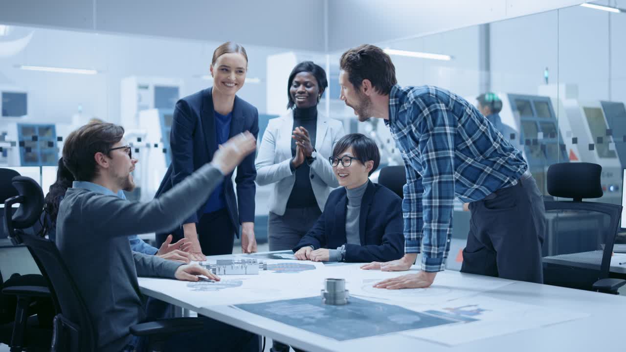Multi Ethnic Team of Industrial Engineers Standing at the Conference Table Successfully Solve Project Problems, They're Happy and Celebrate with High Five and Cheers. Modern Factory. Slow Motion