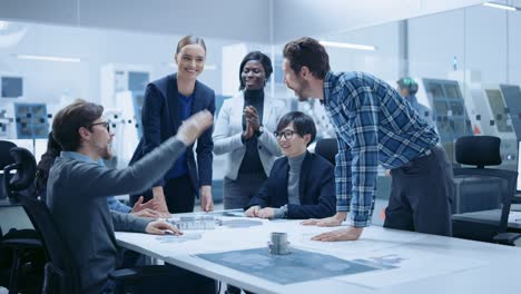 multi ethnic team of industrial engineers standing at the conference table successfully solve project problems, they're happy and celebrate with high five and cheers. modern factory. slow motion