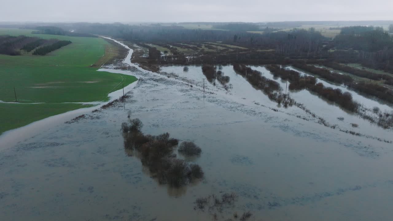 Aerial establishing view of high water in springtime, Alande river flood, brown and muddy water, agricultural fields under the water, overcast day, wide drone shot moving forward