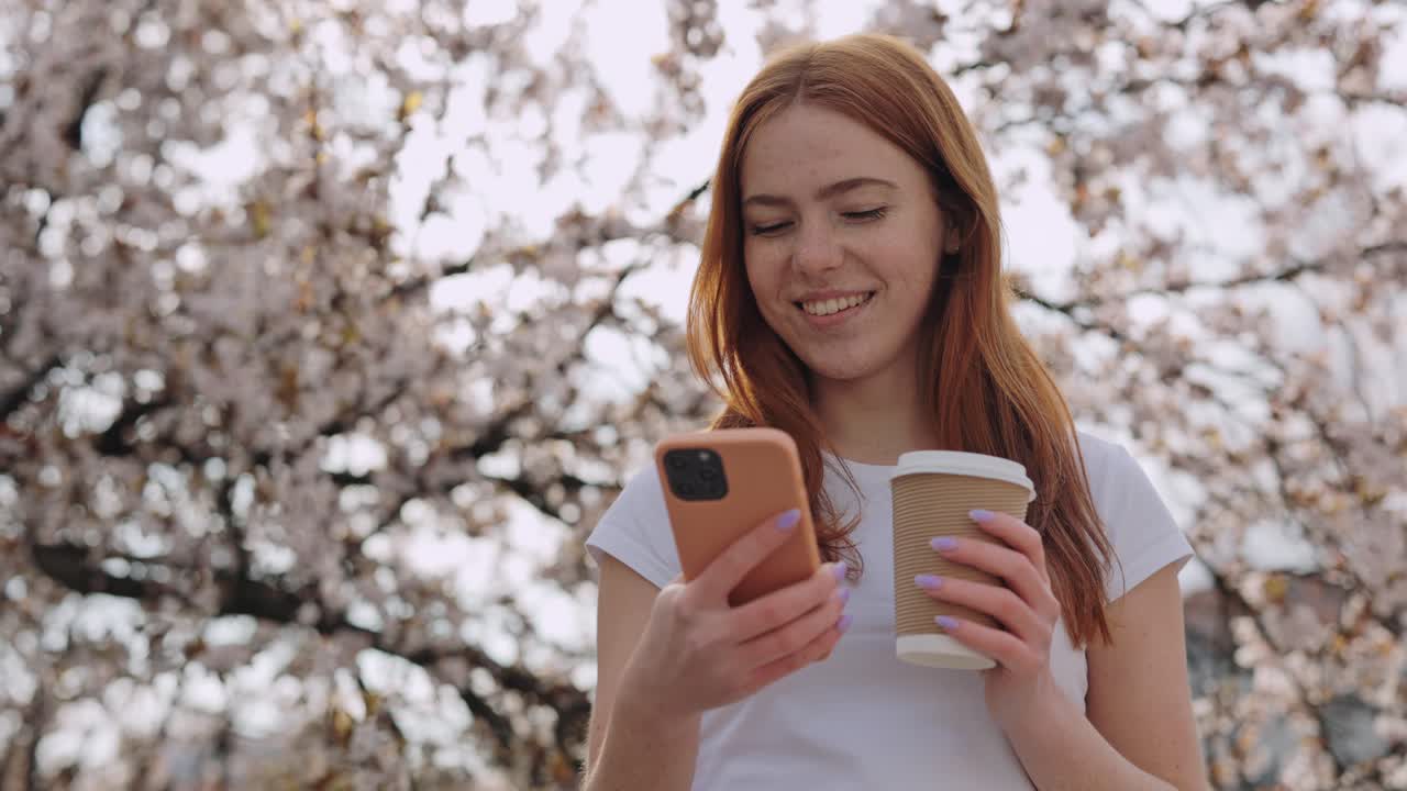 Woman using phone and drinking coffee in a park during spring