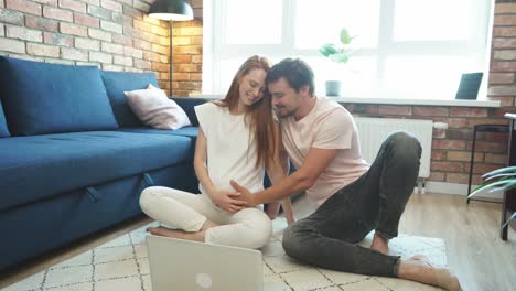 attractive future parents sit on the floor with laptop