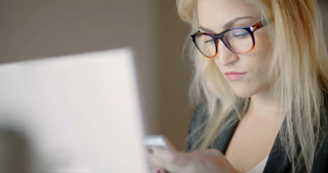 mujer de negocios que usa un teléfono inteligente y mira datos financieros en la computadora portátil 1