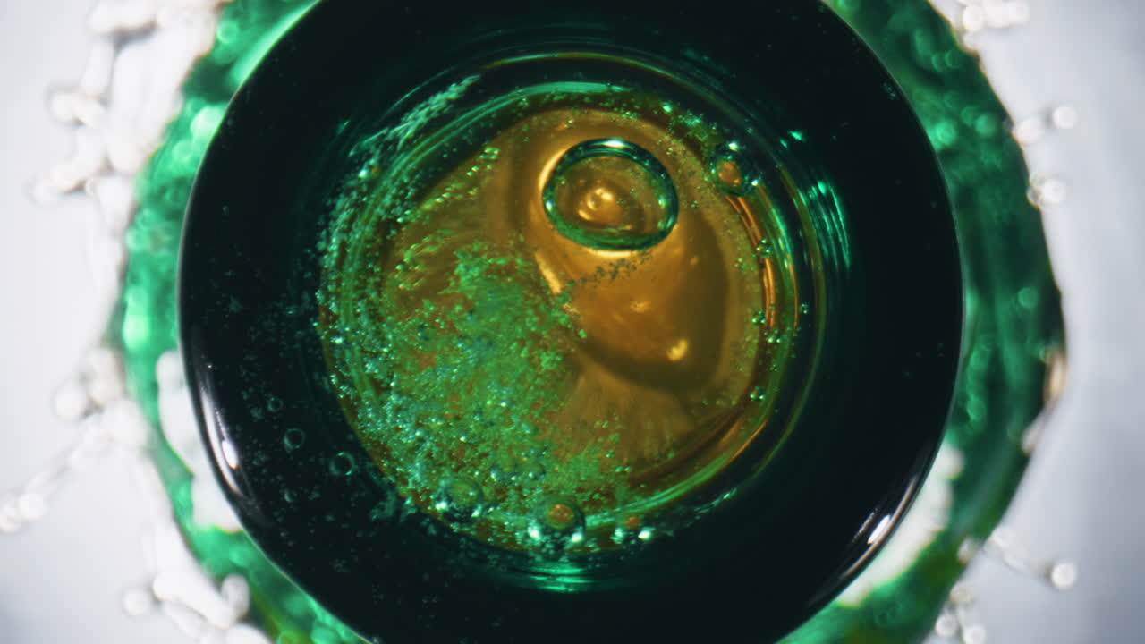Ice cube falling container closeup. Golden ale splashing from flask slow motion