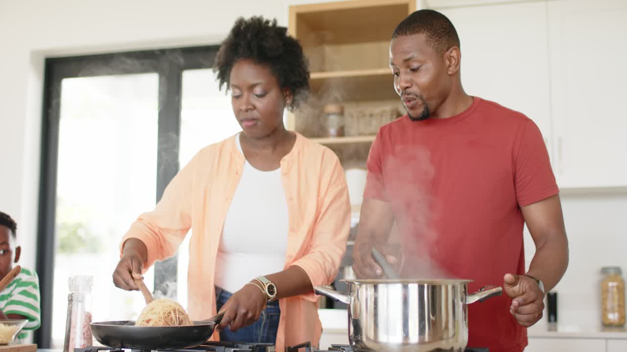 Couple afro-américain cuisinant des pâtes dans une poêle et remuant une casserole pour le dîner sur la cuisinière de leur cuisine à la maison.