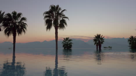 scene with mountains palms and swimming pool at sunset turkey