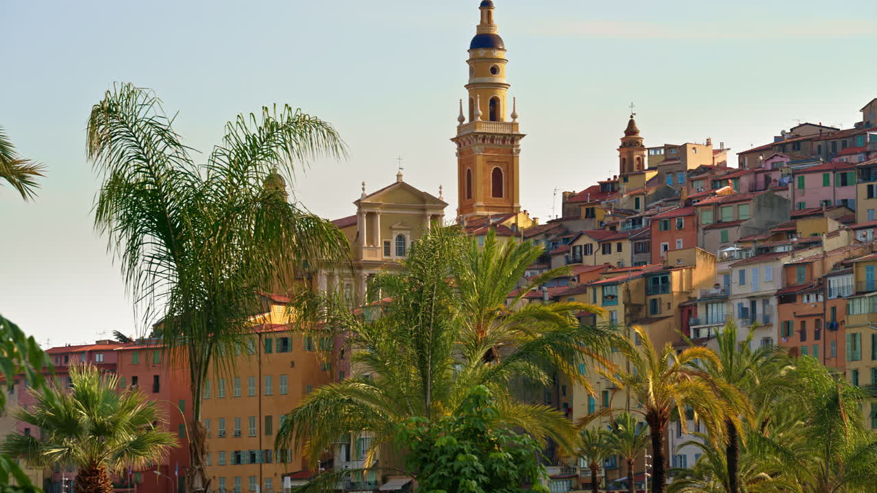 View of palm trees with the colourful buildings in Menton, France on the background