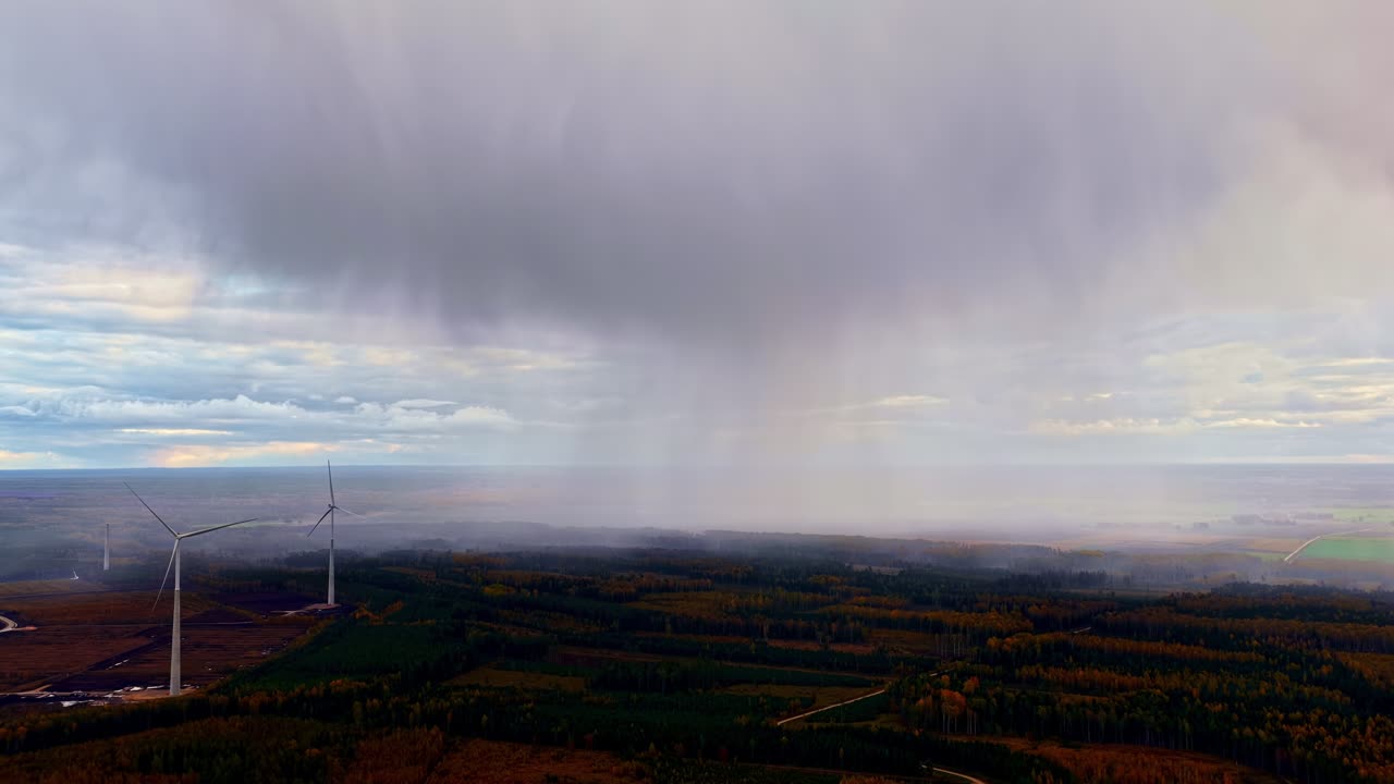 Distant rainfall descends from dark clouds over autumn forests and wind turbines