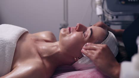 young woman is talking to her cosmetologist while lying on the couch during cosmetic face procedure in spa salon. professional