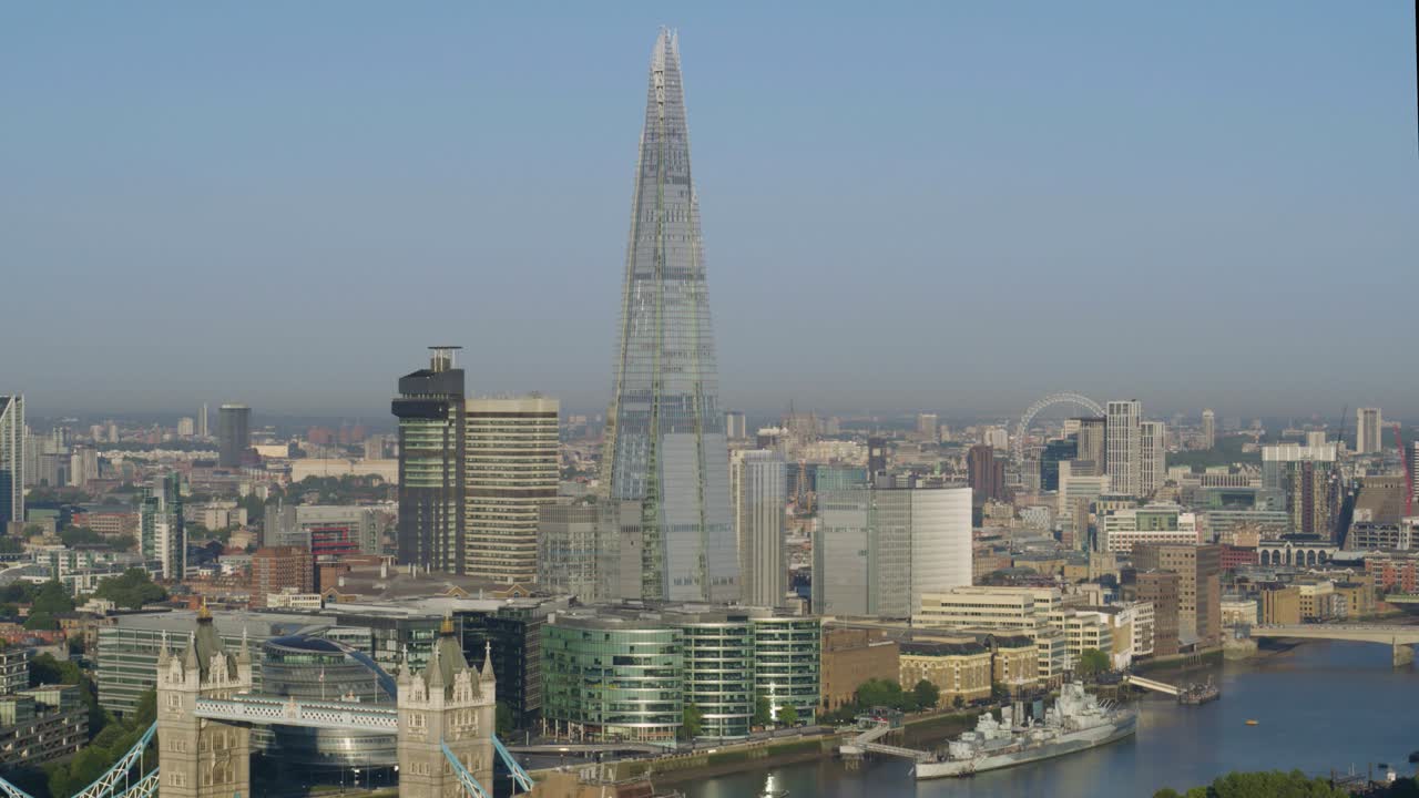 Panning aerial shot of The Shard seen across the River Thames on a peaceful London afternoon. Landmarks HMS Belfast and Tower Bridge can be seen along the river.