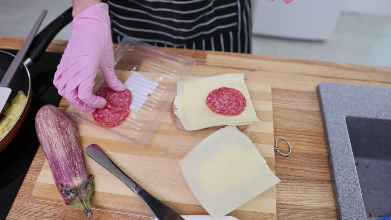 Person preparing a salami and cheese sandwich in the kitchen