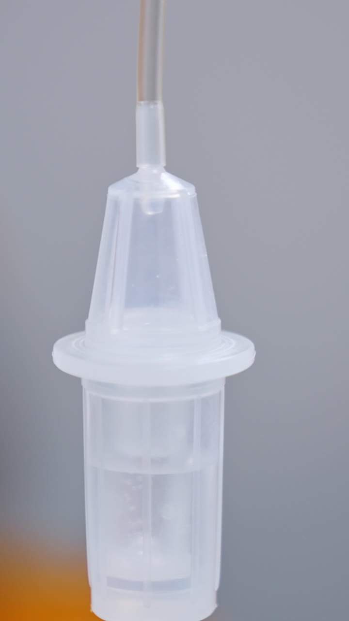 Liquid medicines slowly dripping inside the reservoir of drop counter. Medical equipment close up. Vertical video