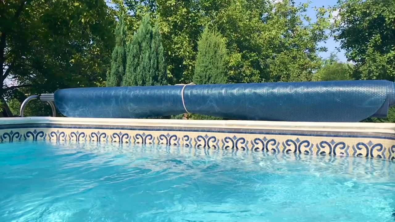Scenic swim pool landscape with trees in the background and closeup of rolled solar pool reel in slow motion