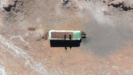 vista aérea superior de un autobús abandonado con dos viajeros en el techo en el desierto de atacama, sudamérica, chile