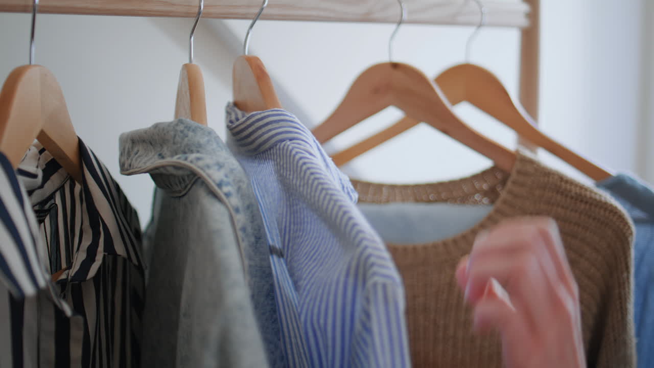 Lady hand taking hanger with blouse in wardrobe closeup. Woman selecting clothes